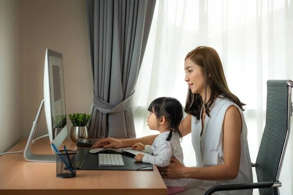 Beautiful happy Asian young mother is using computer and smiling