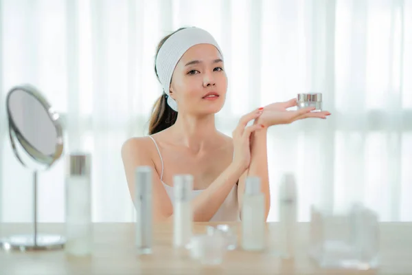 Portrait of Charming Asian woman having jar with face cream in h