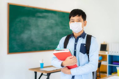 Sırt çantalı ve maskeli Asyalı ilkokul çocuğu Covid 19 'un salgınını önlemek için maskeler takıyor. Okula geri dönerken okullarını yeniden açıyorlar. Eğitim konsepti için yeni bir normal.