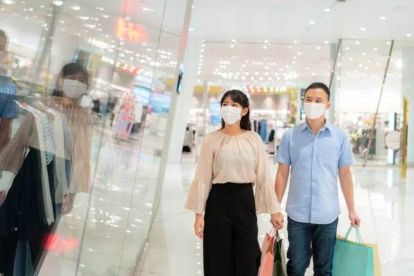アジアのカップル身に着けているマスク彼らの顔の上に新しいコレクションドレスでショッピングモールでショッピングバッグのためのヘルスケアと予防からコロナウイルス 混雑した場所でCovi19インフルエンザ — ストック写真