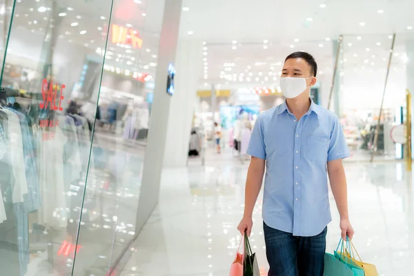 顔の上にマスクを身に着けているアジア人男性は ヘルスケアのためのショッピングバッグやコロナウイルスからの予防とショッピングモールを歩いている間 混雑した場所でCovi19インフルエンザ — ストック写真