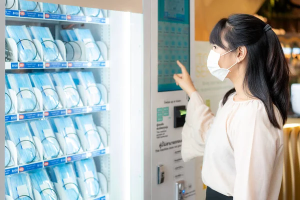 Asian woman wearing mask using mask vending machine to buy mask for protective spreading of disease coronavirus Covid-19 in shopping mall in Bangkok, Thailand.