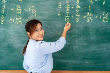Asyalı ilköğretim öğretmeni matematiği karatahtayla anlatıyor uzaktan okulda online ders veriyor e-öğrenim video konferansında sınıftaki kameraya bakıyor..