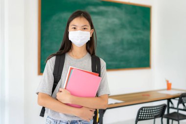 Sırt çantalı ve maskeli Asyalı ilkokul öğrencisi kız Covid 19 'un salgınını önlemek için maskeler takıyor. Okula geri dönerken okullarını yeniden açıyorlar. Eğitim konsepti için yeni bir normal.