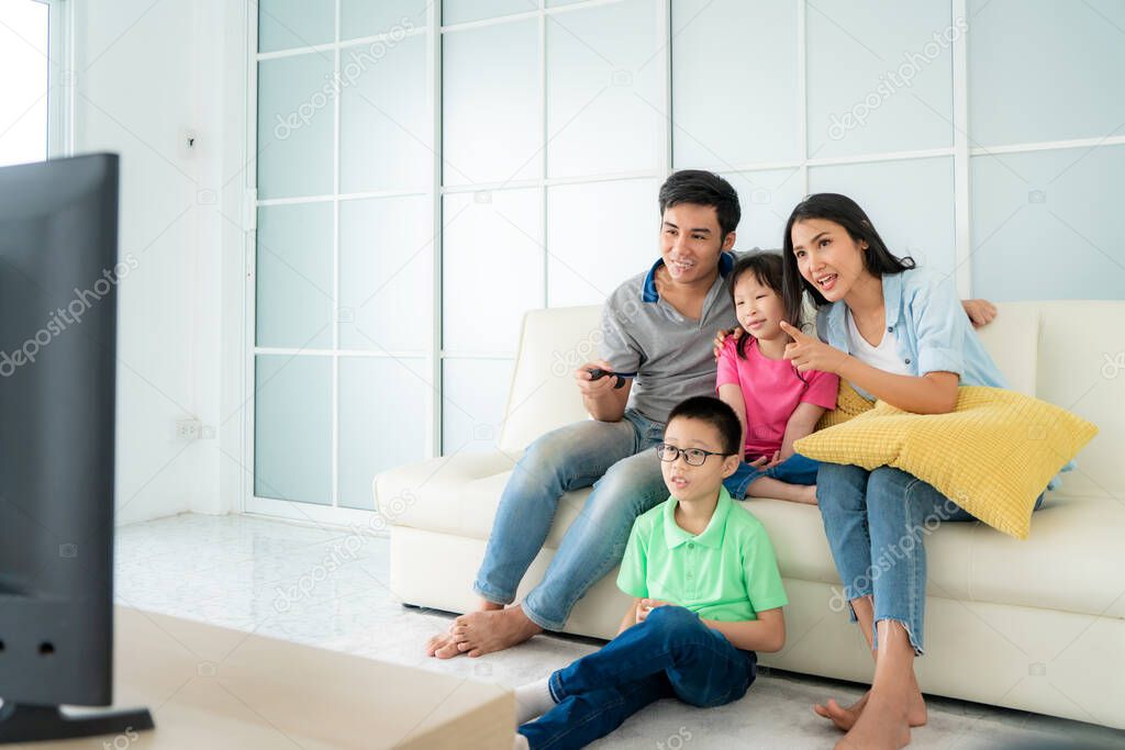 Asian happy family with father, mother, son and daughter sitting in sofa and watching television at home concept of family values, vacation day, holiday, happiness or lifestyle.