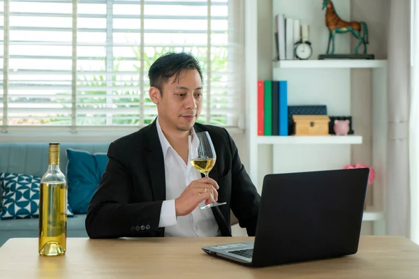 Asian man virtual happy hour meeting party and drinking white grape wine online together with his friend in video conference with digital tablet for a online meeting in video call for social distancing.
