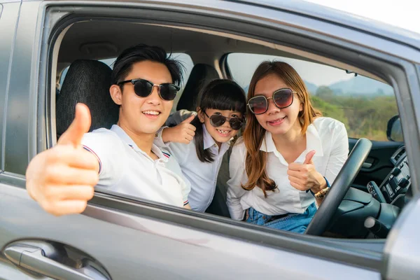 快乐的亚洲家庭带着父亲的大拇指 母亲和女儿在小轿车里戴着防晒霜 他们都在微笑着开车去度假 汽车保险或租金 — 图库照片