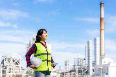 Asyalı kadın mühendis elinde beyaz bir kaskla petrol rafinerisi fabrikasının geleceğinin planını tutuyor.. 