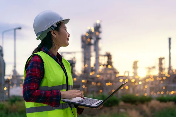 Asian woman petrochemical engineer working at night with laptop Inside oil and gas refinery plant industry factory at night for inspector safety quality control