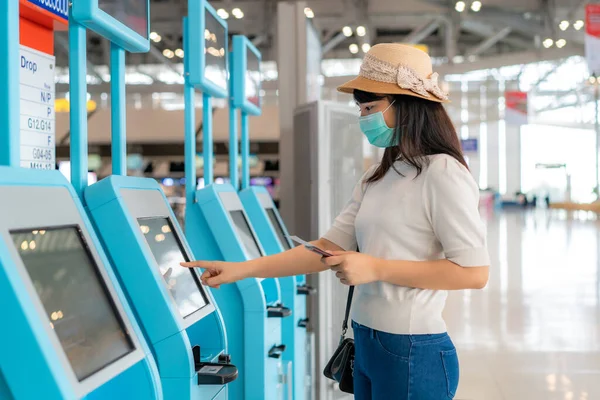 海外旅行の際には コロナウイルス Covid のパンデミック予防のために 空港ターミナルのセルフチェックインキオスクを使用してマスクを着用するアジアの女性旅行者 新しい通常の旅行コンプ — ストック写真