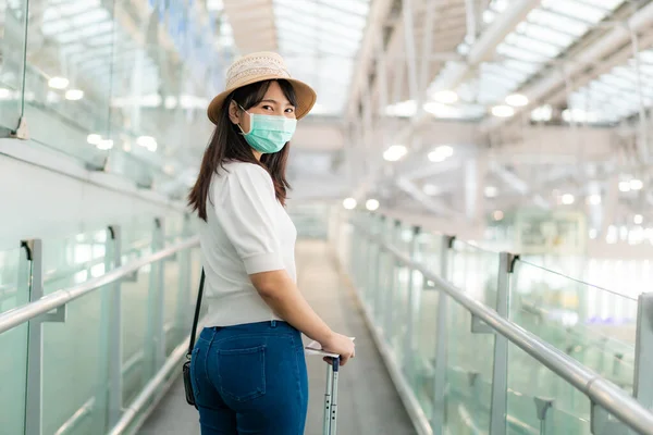 アジアの女性旅行者は 空港ターミナルに立ってカメラと笑顔を見てボードに顔をマスクを歩く姿 新しい通常の旅行コンセプトのための飛行機輸送で旅行する女性の乗客 — ストック写真