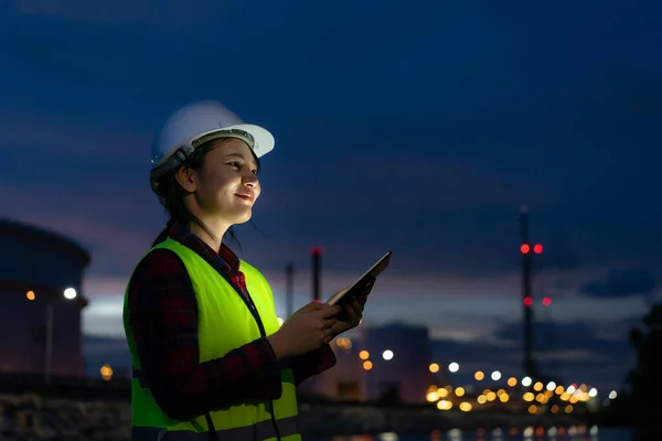 亚洲女石油化工工程师在夜间与数字平板电脑一起工作石油和天然气精炼厂内部的工厂在夜间进行检查员安全质量控制 — 图库照片