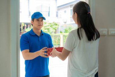 Asyalı teslimatçı, mavi üniformalı, elinde pizza kutuları olan genç adam ve teslimatçıdan gelen pizza kutularını kabul eden Asyalı kadın. Reklamcılık, İş, Ulaşım.