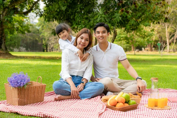 アジアのティーン家族の幸せな休日のピクニック瞬間公園で父 母と娘と一緒にカメラと笑顔で幸せな休暇の時間を過ごすために緑の庭で果物と食べ物 — ストック写真