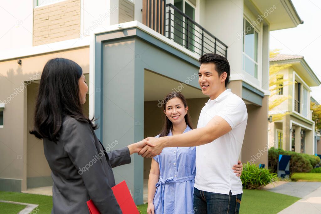 Happy Asian couple looking for their new house and shake hands with real estate broker after a deal. Young couple handshaking real estate agent after signing contract for buy house