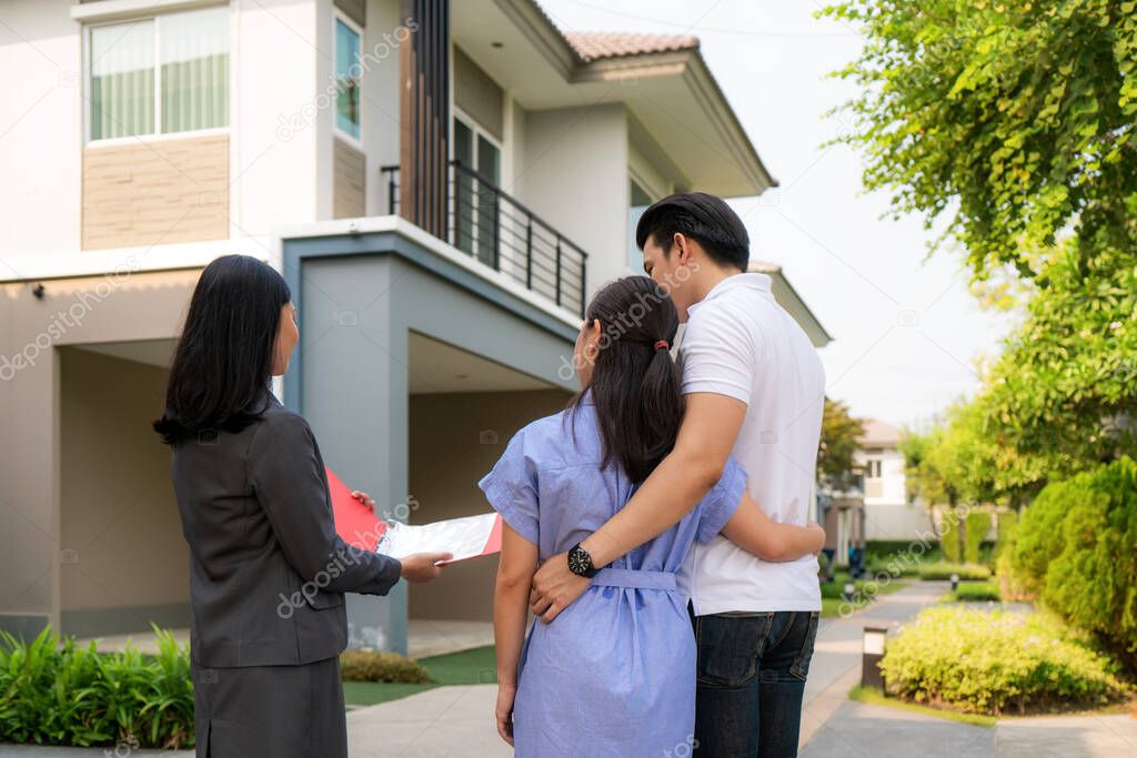 Asian woman Real estate broker agent showing a house detail in her file to the young Asian couple lover looking and interest to buy it. Buying a new house