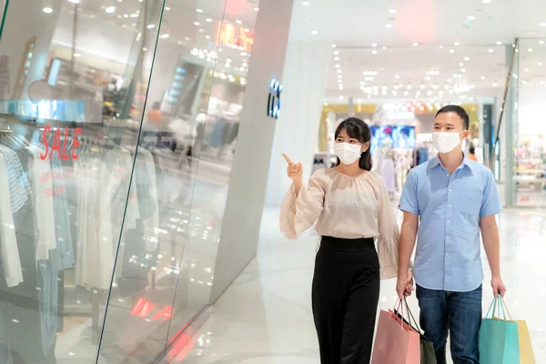 アジアのカップル身に着けているマスク彼らの顔の上に新しいコレクションドレスでショッピングモールでショッピングバッグのためのヘルスケアと予防からコロナウイルス 混雑した場所でCovi19インフルエンザ — ストック写真