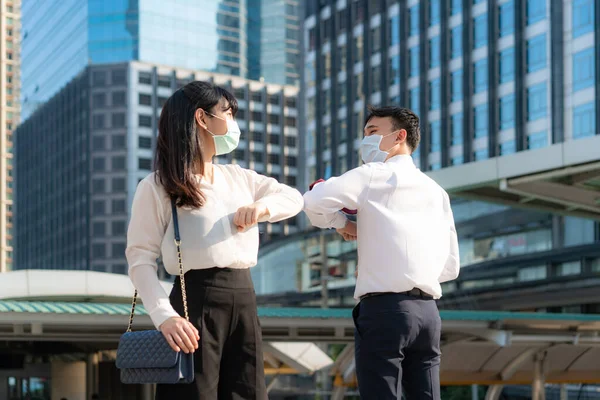 Elbow bump is new novel greeting to avoid the spread of coronavirus. Two Asian business friends meet in front of office building. Instead of greeting with a hug or handshake, they bump elbows instead.