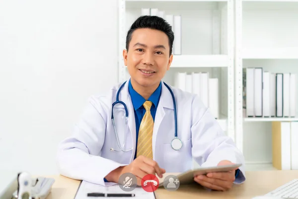 Smiling Asian doctor with digital tablet looking at camera. Remote online medical chat consultation, tele medicine distance services, virtual physician conference call, telemedicine concept.