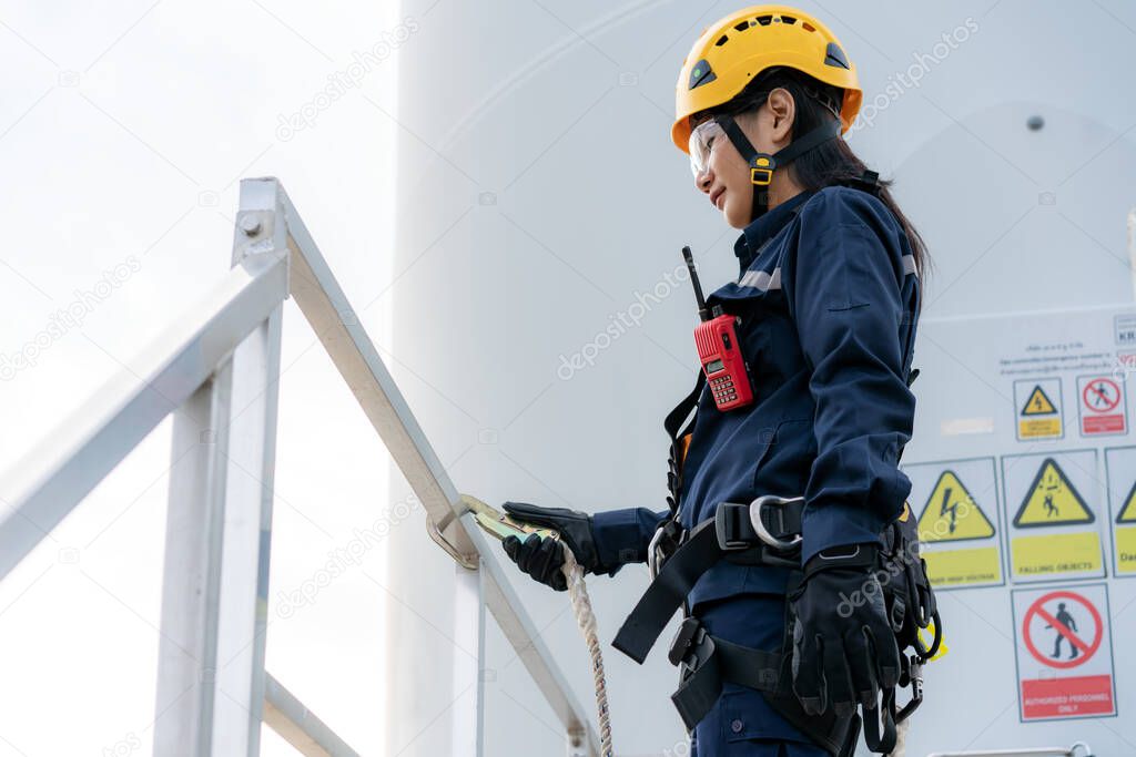 Asian woman Inspection engineer wearing safety harness and safety line working preparing and progress check of a wind turbine with safety in wind farm in Thailand.