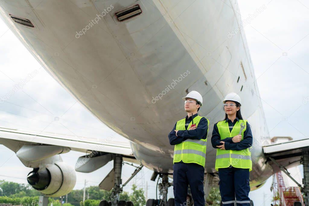 Asian man and woman engineer maintenance airplane arm crossed and holding wrench in front airplane from repairs, fixes, modernization and renovation in airport