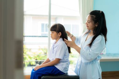 Asyalı anne, evde okula gitmeden önce sabah kızının saçını tarıyor. Sabah okulunun günlük rutini okula hazırlanmak.