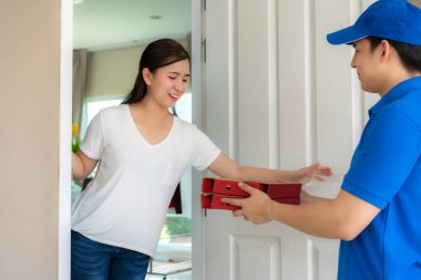 Asyalı teslimatçı, mavi üniformalı, elinde pizza kutuları olan genç adam ve teslimatçıdan gelen pizza kutularını kabul eden Asyalı kadın. Reklamcılık, İş, Ulaşım Konsepti.