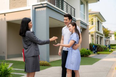 Asyalı mutlu bir gülümseme genç çift emlakçıdan ya da emlakçıdan evinin önündeki yeni büyük evin anahtarlarını alıyor. Sözleşme anlaşması imzaladıktan sonra, gayrimenkul konsepti, eve taşınma ya da mülk kiralama gibi.