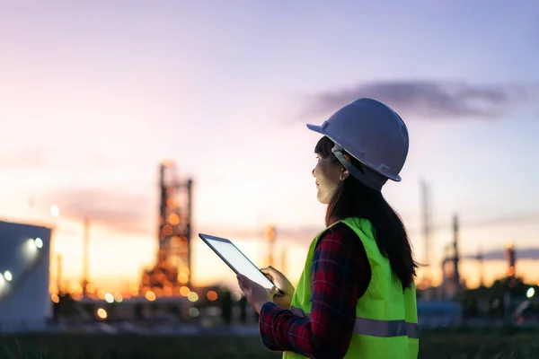 Asian woman petrochemical engineer working at night with digital tablet Inside oil and gas refinery plant industry factory at night for inspector safety quality control