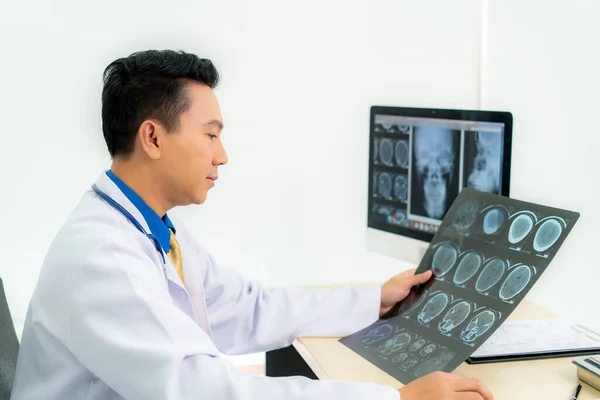 Asian man doctor holding and looking to examining x ray of the patients skull and brain in a medical clinic at hospital.