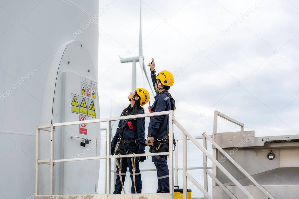 Asian man and woman Inspection engineers preparing and progress check of a wind turbine with safety in wind farm in Thailand.