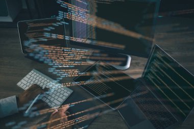 Kodlama ve yazılım geliştirme kavramı, programcı dizüstü bilgisayar, tablet ve ekranda parlayan kod satırlarını göstererek klavyede yazarken.