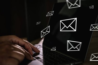 Yüzen e-posta simgeleri, dijital iletişim konsepti, çevrimiçi mesajlaşma, e-posta pazarlaması ve İnternet teknolojisi içeren dizüstü bilgisayarda yazı yazan ellerin yakın plan görüntüsü.