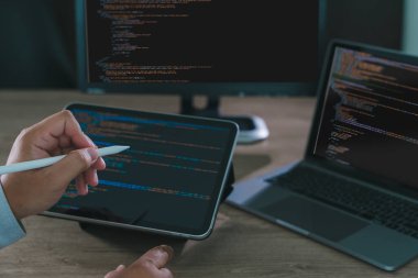 Ekranda kod, modern yazılım geliştirme, kodlama ve ev ofis ortamında uzaktan çalışma ile birlikte tablet ve dizüstü bilgisayar üzerinde çalışan programcı serbest çalışmalarına yakın plan.