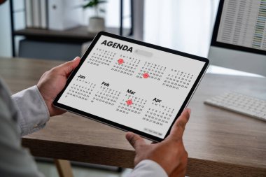 İş adamlarının elinde dijital ajanda takvimi olan bir tablet, kırmızı tarih işaretleyicileri ve modern bir toplantı programı ofisinde aylık görünümü olan bir tableti kapatması, zaman yönetimi