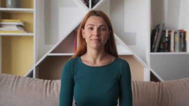 Gülümseyen güzel kadın kameraya bakıyor koltukta tek başına oturuyor ve el sallıyor.