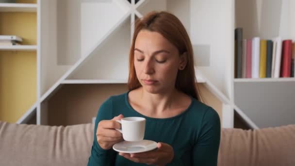 Junge Frau sitzt auf Sofa und genießt erholsamen neuen Tag beim Kaffeetrinken zu Hause — Stockvideo