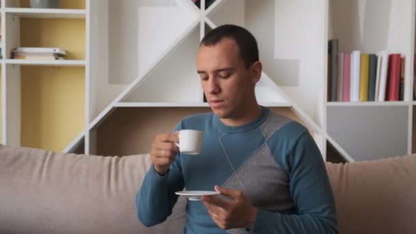 Ung man sitter på soffan njuter av fräsch ny dag känsla utvilad dricka kaffe hemma — Stockvideo