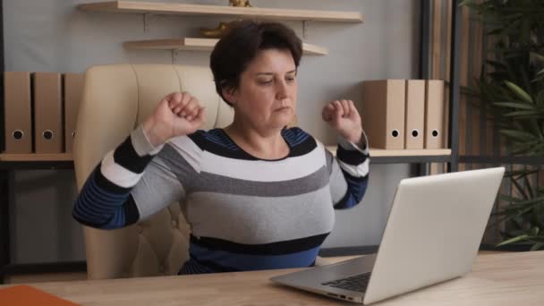 Die Frau ist es leid, am Computer zu sitzen und zu arbeiten. Sie streckt sich auf dem Stuhl und zieht sich hoch. Bleiben Sie zu Hause. — Stockvideo