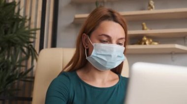 Coronavirus karantinası. Ofiste Corona virüsü maskeli bir kadın var. İş kadınları sağlıklarını korumak ve korumak için maske takarlar. Evde bilgisayarla çalışıyor. Evden çalışmak