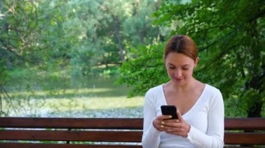 Genç bayan telefonuna bakar ve parkta gülümser..