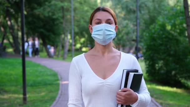 Porträtt Studentflickan står ensam i en park i mask under epidemin. Säkerhet, avstånd, hälsa, N1H1, virusskydd, covid, virus och coronavirus. — Stockvideo