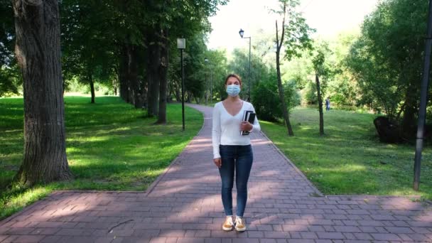 한 여학생이 유행하는 동안 마스크를 쓴 채 공원에 홀로 서 있습니다. 안전, 거리, 건강 , N1H1, 바이러스 보호, 코로나 바이러스 및 코로나 바이러스 개념. — 비디오