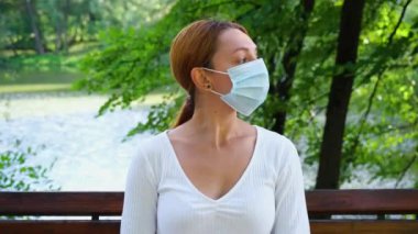 Genç bir kadının portresi salgın sırasında parkta tek başına oturuyor. Güvenlik, mesafe, sağlık, N1H1, virüs koruması, covid, virüs ve koronavirüs kavramı