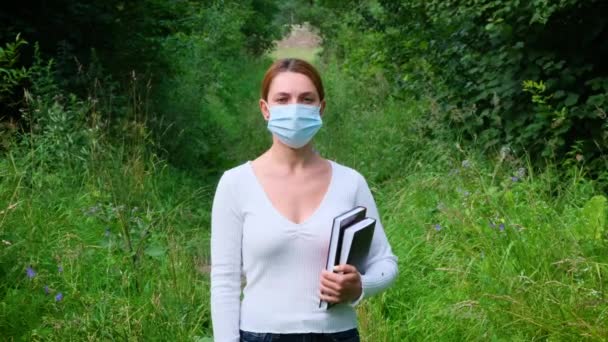 Portrétní mladá žena stojí sama v parku v masce. Bezpečnost, vzdálenost, zdraví, N1H1, ochrana virů, kovid, virus a koronavirus koncept. — Stock video