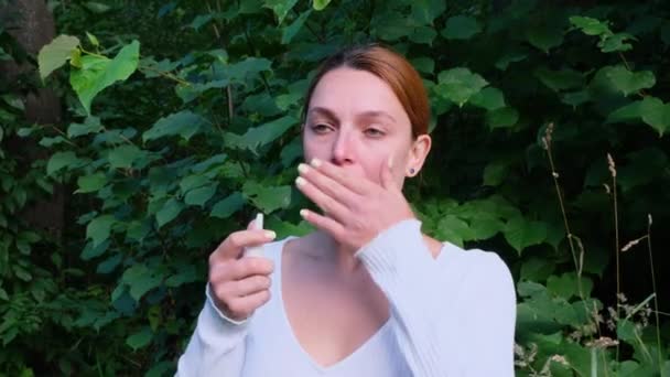 Giovane donna che indossa sciarpa rossa spruzzando spray nasale in piedi nel parco cittadino. Concetto di terapia sanitaria Concetto. Medicina. — Video Stock