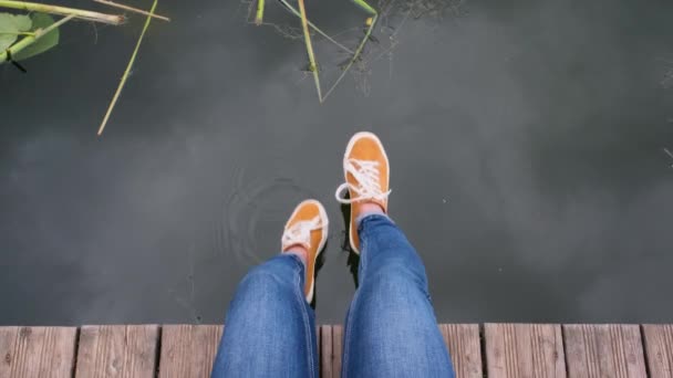 POV zastřelil mladou ženu sedící na molu u jezera. jen nohy — Stock video