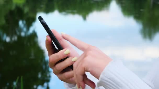 Cerca de las manos de mujer utiliza el teléfono en el fondo del parque . — Vídeos de Stock