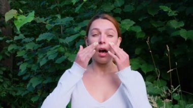 Genç bir kadın hapşırır ve çiçek açan ağacın yanında durup burnunu ovuşturur. Alerjik rhinitis hastası. Alerji konsepti.