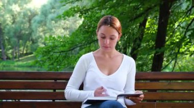 Güneşli yaz gününde parkta kitap okuyan genç bir kadın. Hoş bir bayan hafta sonu parkta dinleniyor, kitap okuyor ve günışığının tadını çıkarıyor..